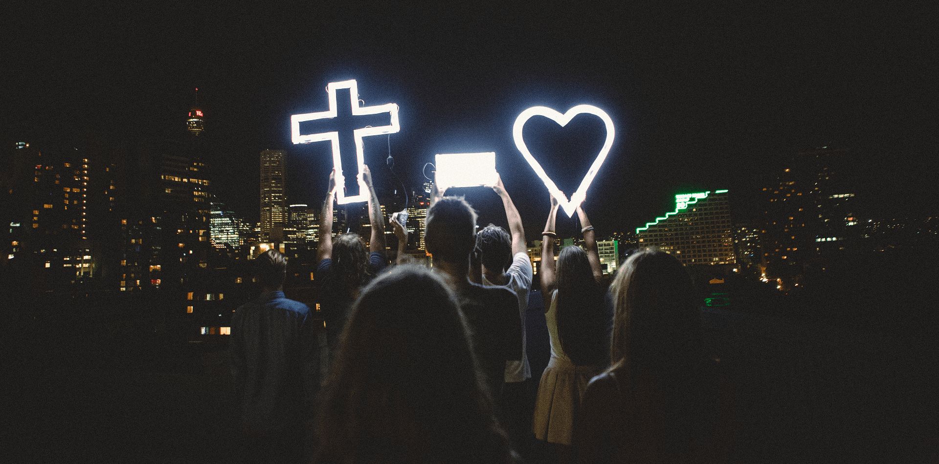 A crowd at night holding up a lit cross and a lit heart