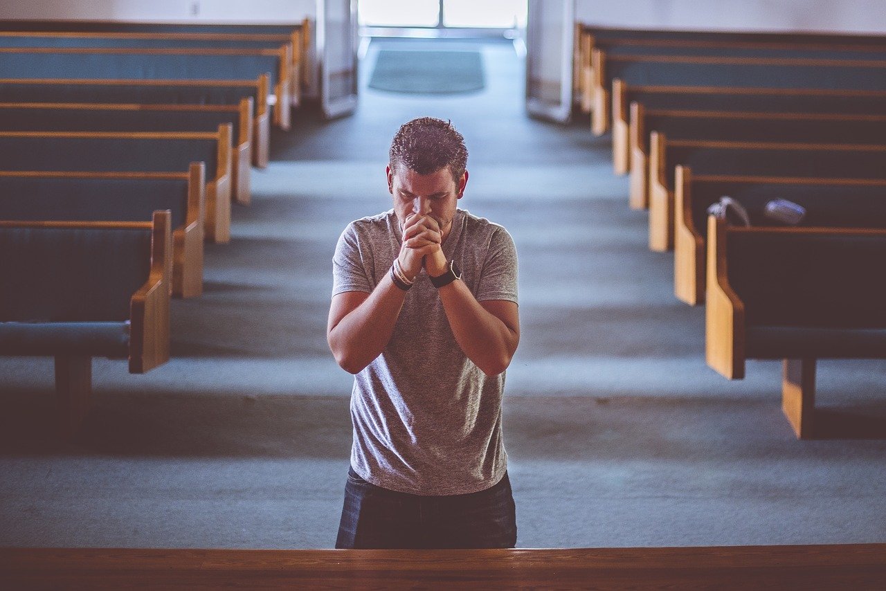 A person standing alone in prayer between empty church pews