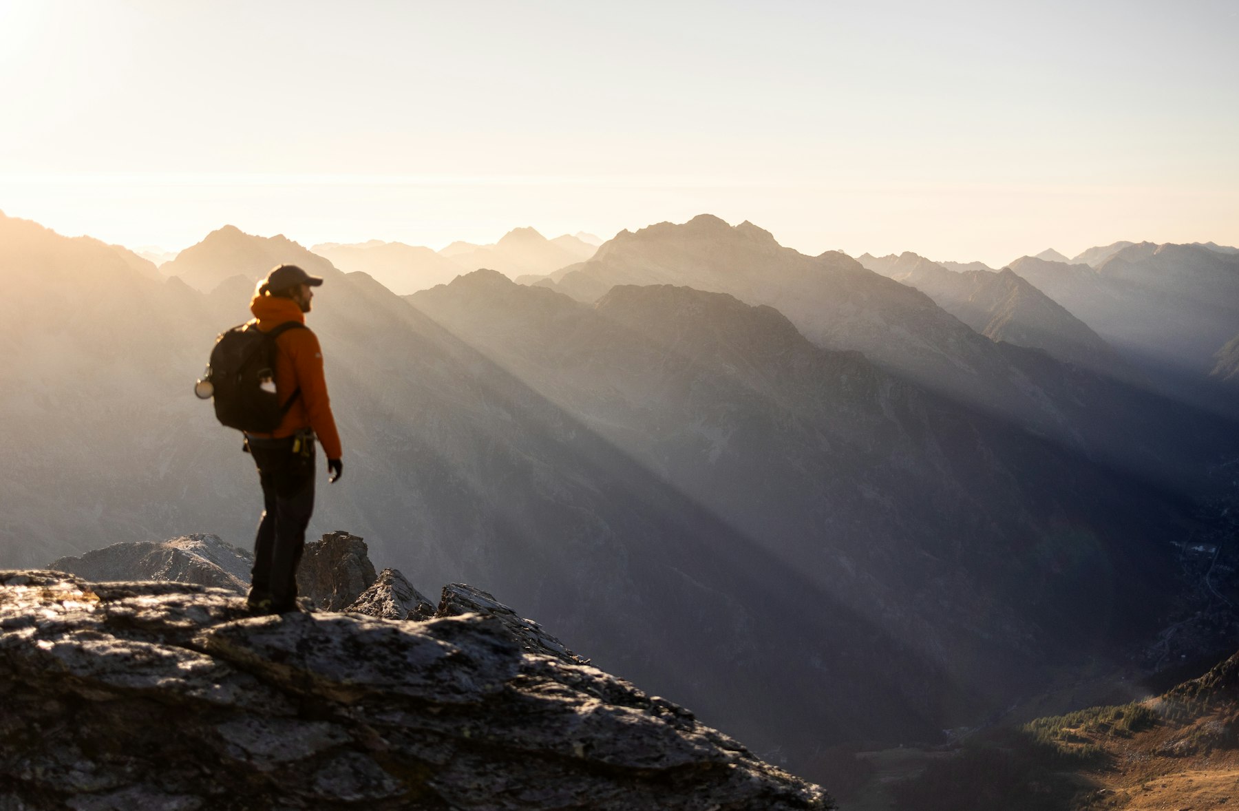 A hiker standing on a rocky peak as the sunrise breaks over the mountains